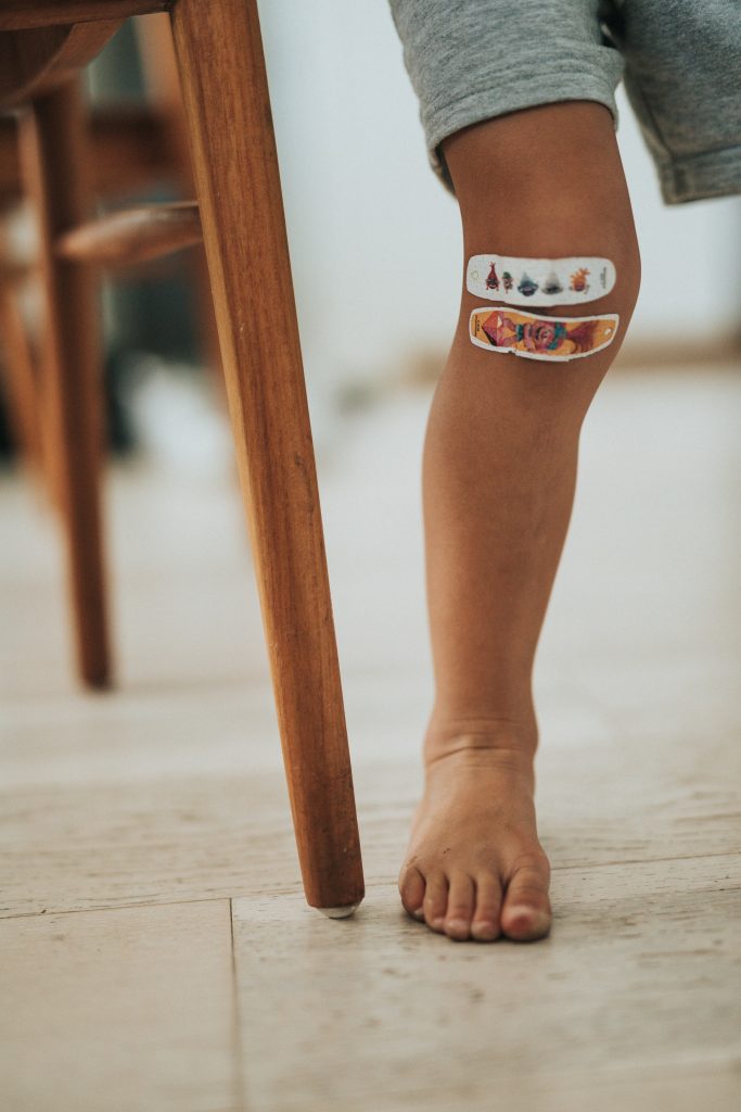 Child wearing two bandages on their knee.