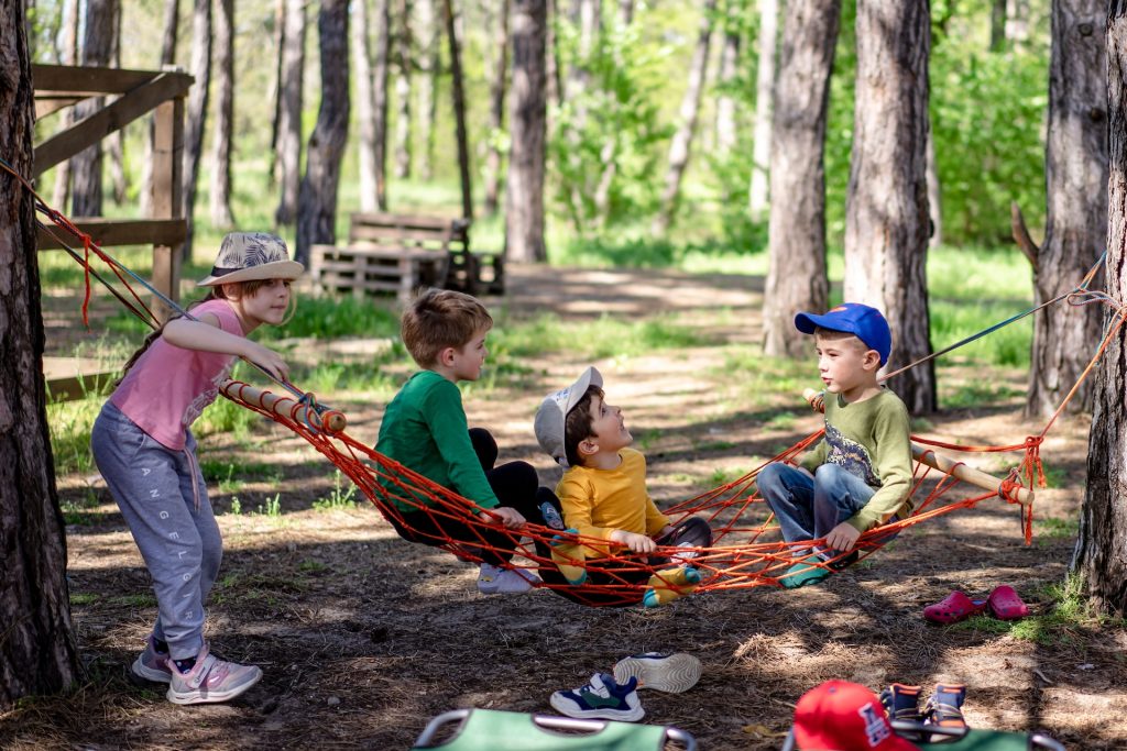 A group of kids sitting in a hammock in the woods.