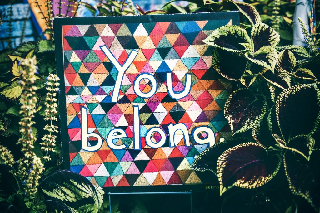 A sign that says "you belong" surrounded by plants.