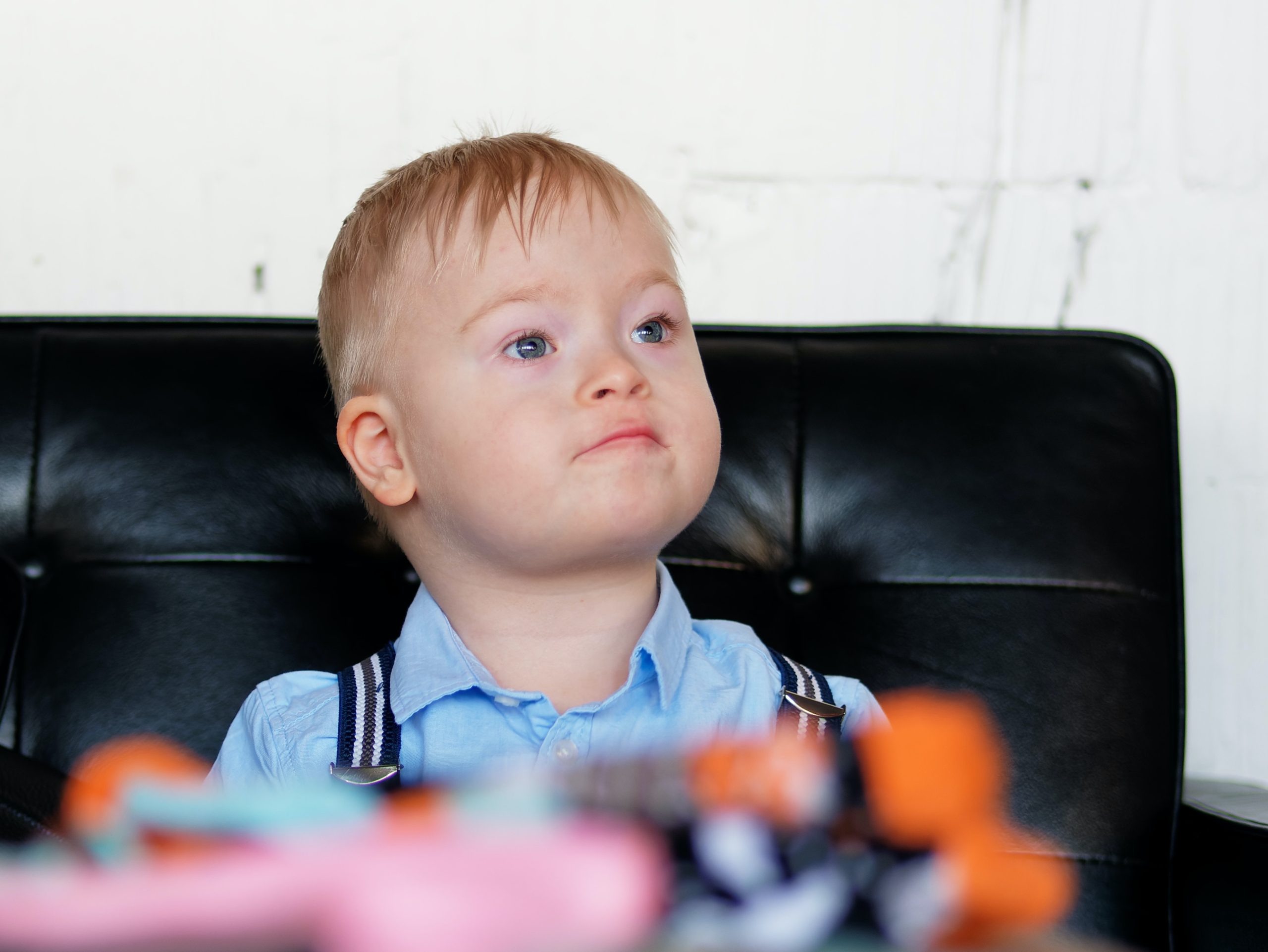 A young boy with Down syndrome sitting in a black chair.