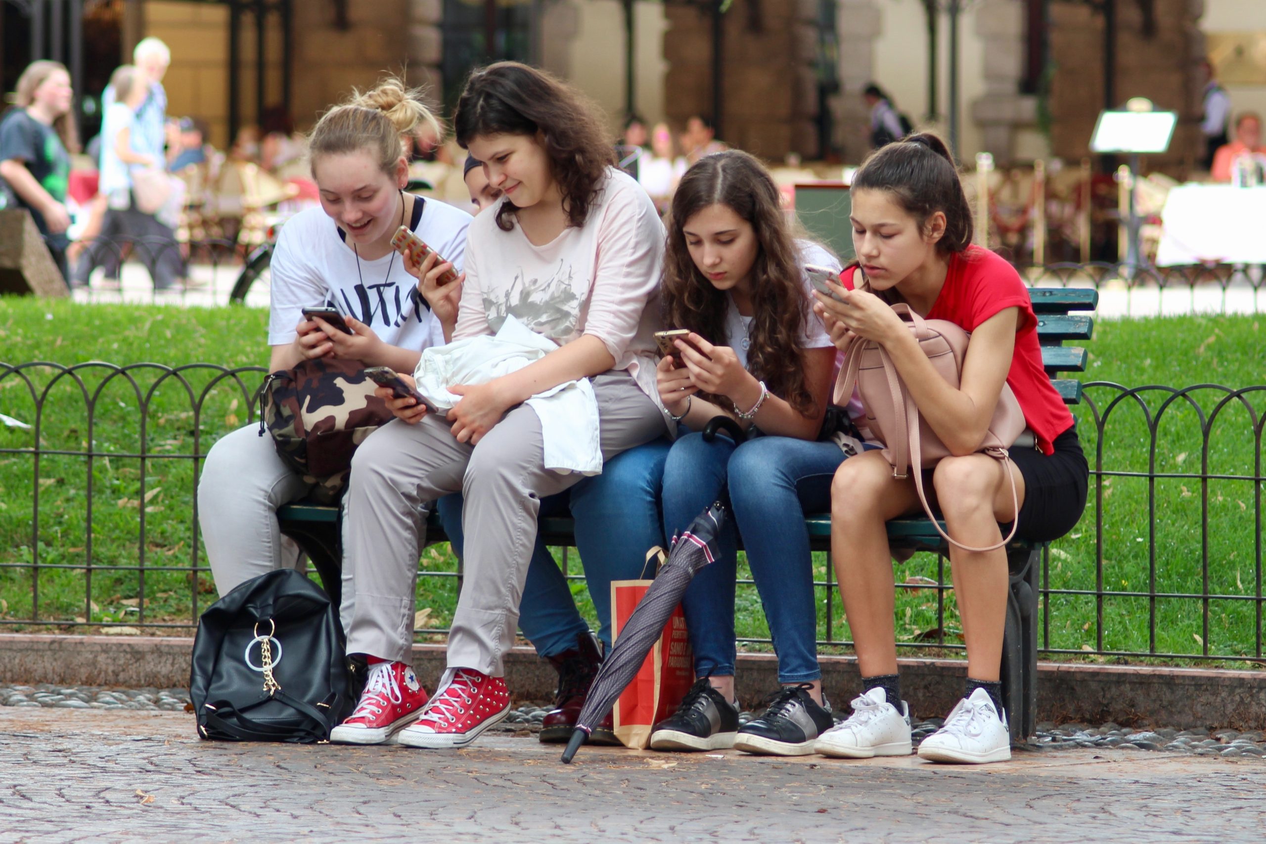 Students sitting on bench each using a cell phone