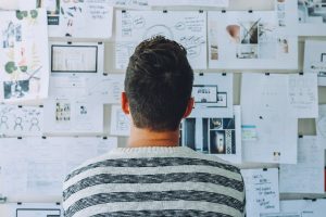 Man standing before a board with ideas and notes taped up.