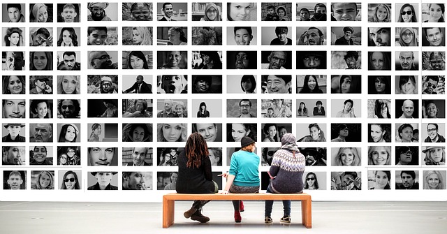 Three people sitting on a bench before a wall of photographs.