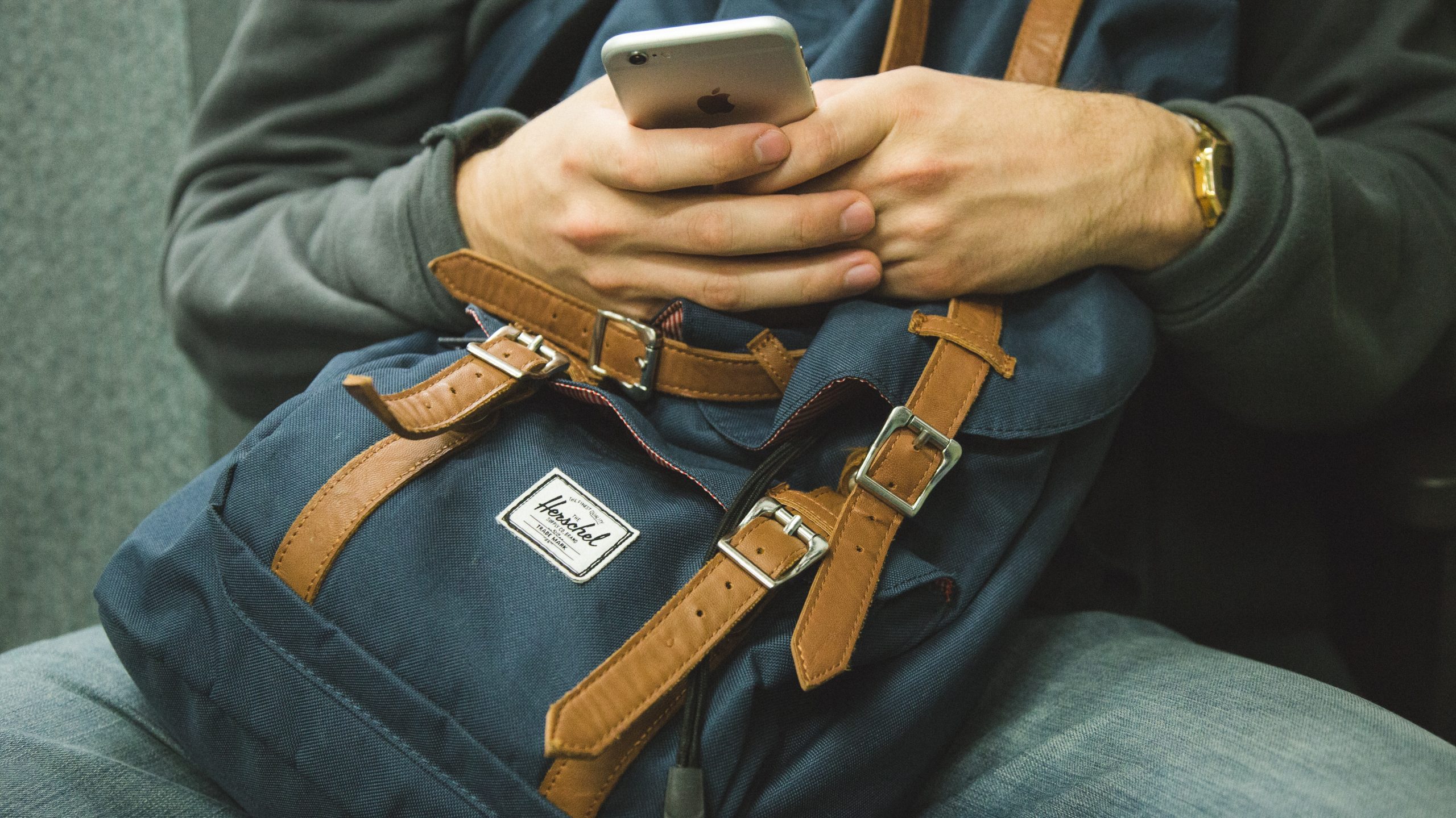 Man sitting on a chair with a backpack, checking his mobile.