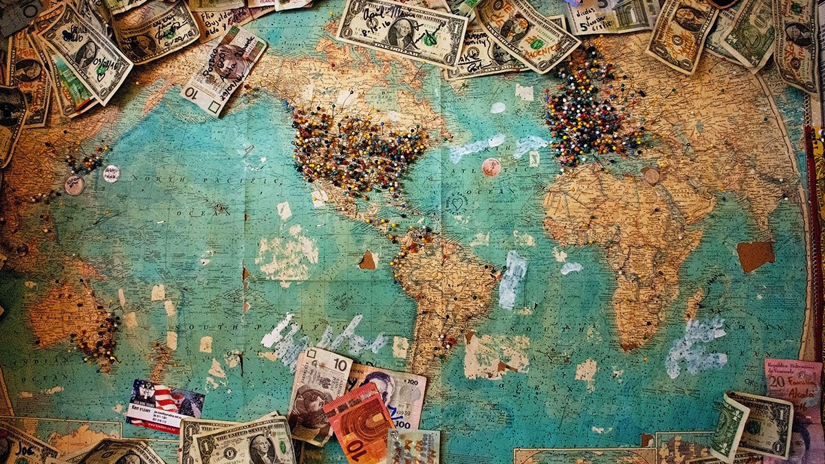 The image illustrates the map of the world with money and pins attached to it