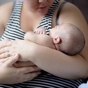 A young mother holds an infant in her arms." title="A young mother holds an infant in her arms.