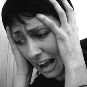 A woman holds her hands to the sides of her head and looks down with an expression of panic.