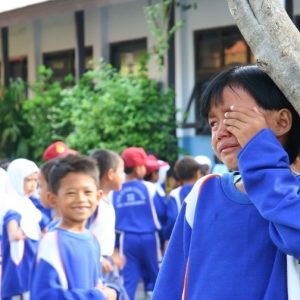 A boy stands crying on the playground as another boy looks on smiling.