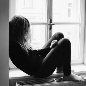 A young women sits alone on a windowsill.