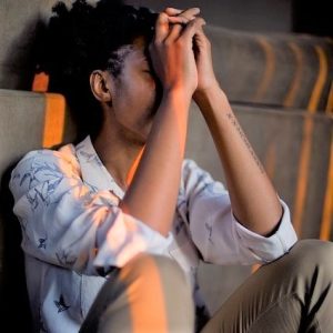 A woman sits on the floor and covers her face in sadness.