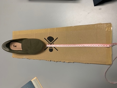 shoe placed on a cardboard ramp with a measuring tape measuring the distance from the toe of the shoe to the bottom of the ramp.