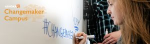 Person writing the word #changemaker on a white board in blue marker.