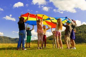 A group of children work together to lift a multicoloured parachute on a bright sunny day.