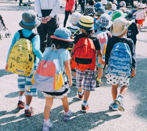 A group of children walking in a large group with backpacks on.