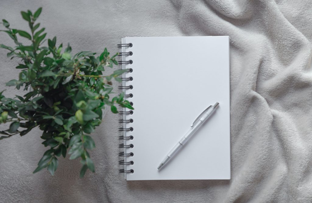 A school, office notebook with a white pen and green branches lies on a gray table, desk, background.