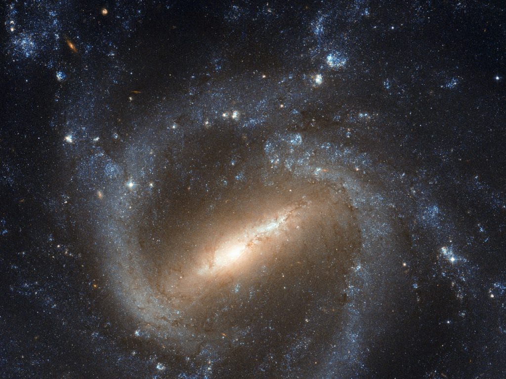 Image of a Barred-Spiral Galaxy. Just below center is the elongated central bar tilted about 45-degrees from the bottom of the frame. At each end of the bar begin the spiral arms, twisting clockwise around the central bar and encircling the whole galaxy.