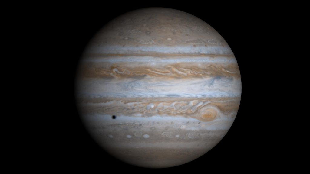 Photograph of Jupiter. Taken from the Cassini spacecraft, the alternating light and dark cloud bands are visible over the entire planet. The Great Red Spot is at lower right. Also seen is the shadow of the moon Europa at lower left.