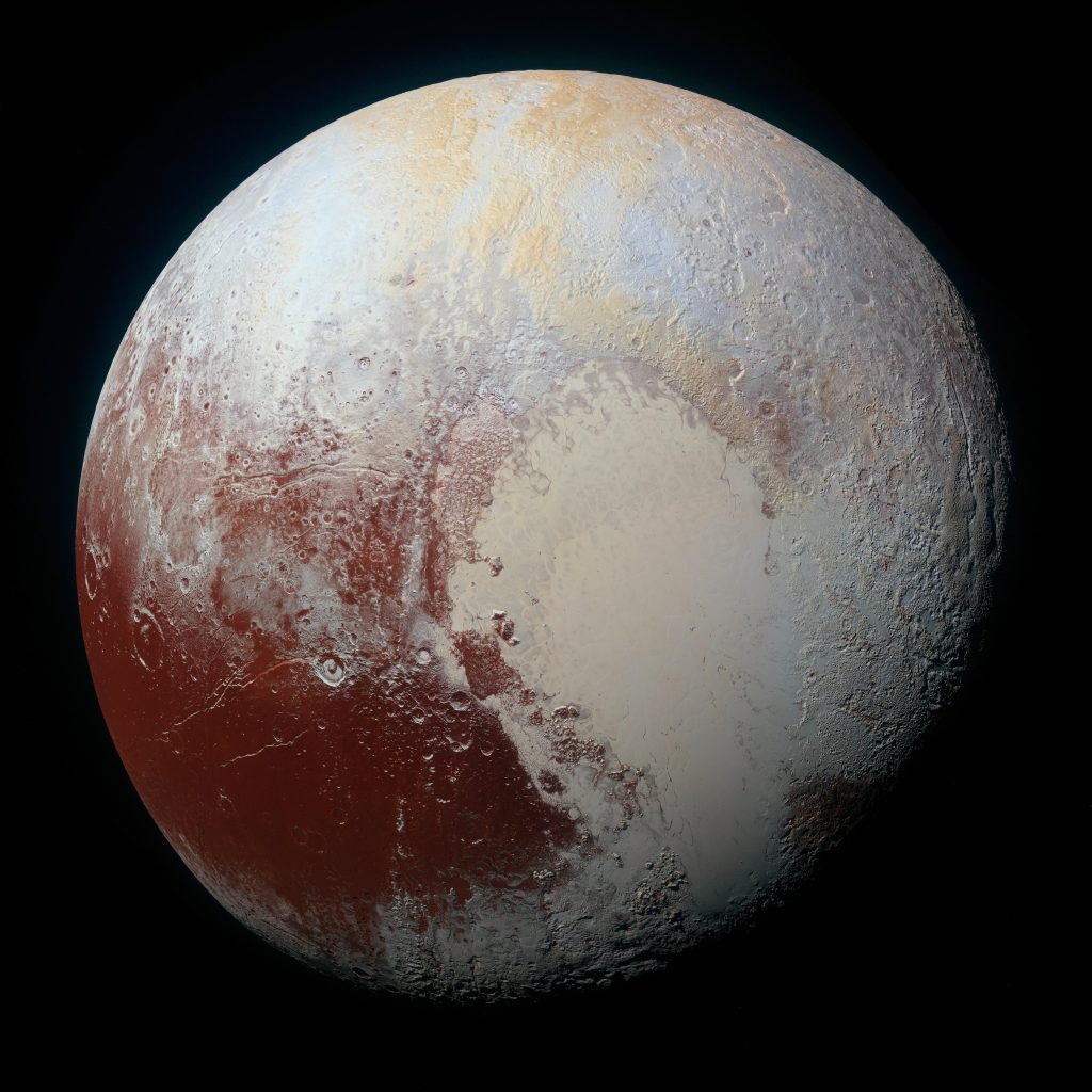 A global colour image of Pluto, showing a dark area in the lower left covered with impact craters, and a larger light area in the centre and lower right that is flat.