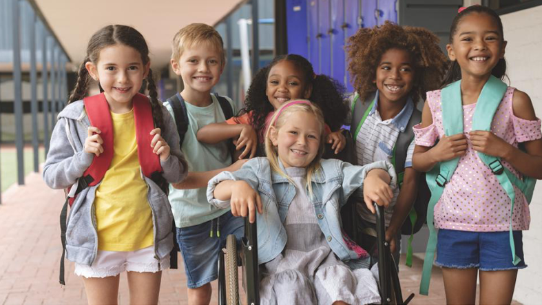 A group of children standing in a school hallway; one of the children is sitting in a wheelchair.