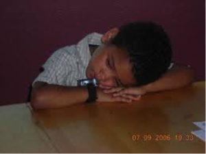 A young child rests his head on his arms on a tabletop.