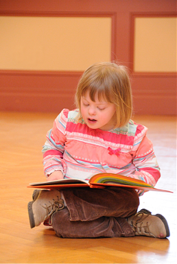 A young girl sitting cross-legged on the floor looking at a book.