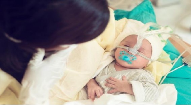 A small baby wrapped in blankets has tubbing attached to their nose.