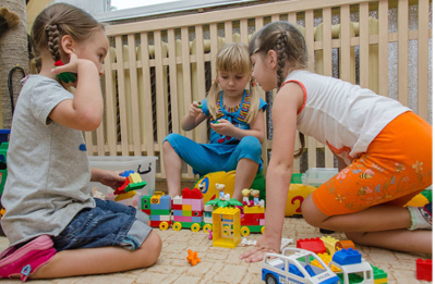 Three children are outside playing on a patio with Lego blocks.