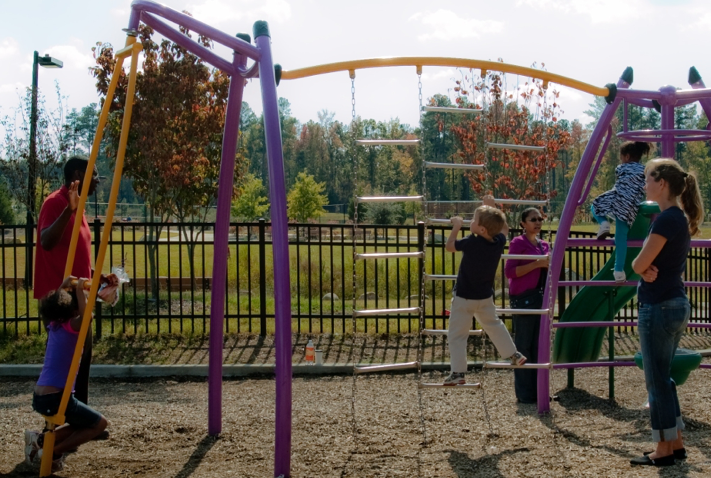 Adults observe children playing on a swing set at a playground.