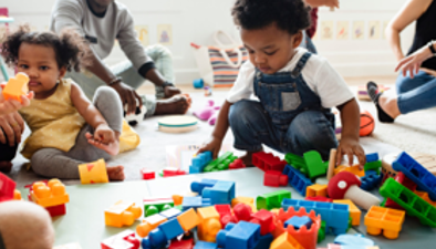 Two children are sitting amongst large lego toys.