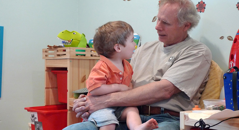 A man sits with a child in his lap and is talking to him.