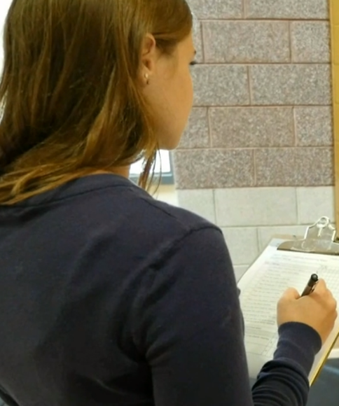 A young woman holds a clipboard and pen.