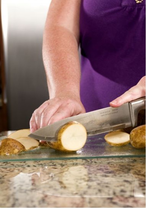 A person uses a knife to cut a potato on a glass cutting board.