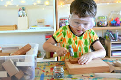 A young boy wears safety goggles and uses a toy hammer.