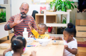 A man sits at a table with three children as they eat cereal.