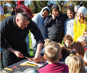 A chef preparing food outdoors on a table in front of children.
