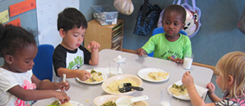 A group of young children sit around a table eating food.