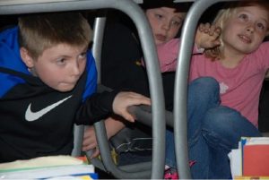 Three young children are hiding under a table.