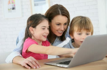 An woman with a child on either side of her all look at a laptop; one child is pointing at the screen.