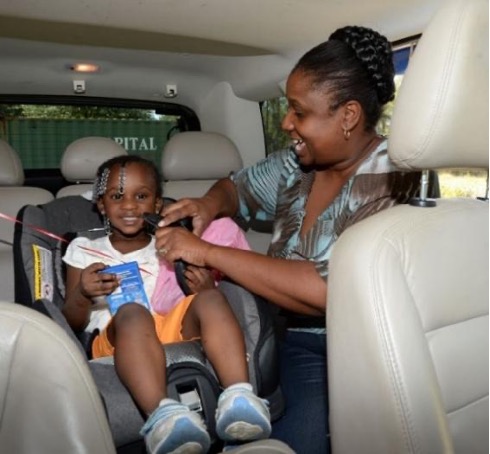 An adult is buckling a young girl into their carseat in the back of a vehicle.