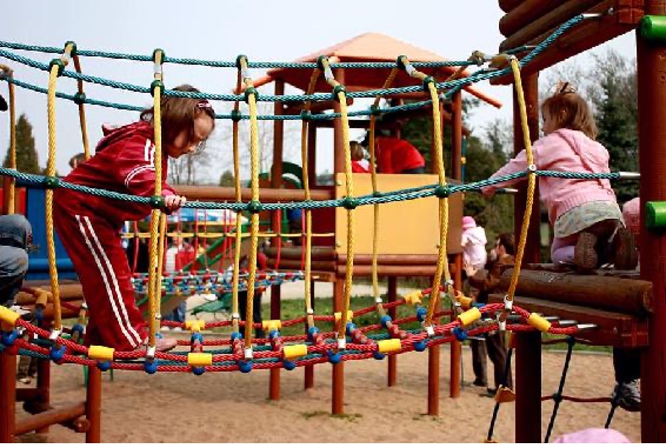 Children cross a bridge made of ropes at an outdoor playground.