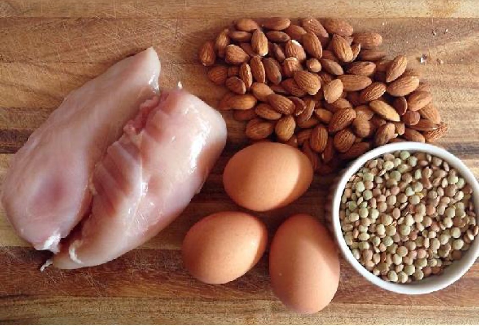 Nuts, legumes, eggs, and chicken lay on a wooden board.