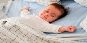 A baby sleeps with their arms outstretched and a blanket over them.