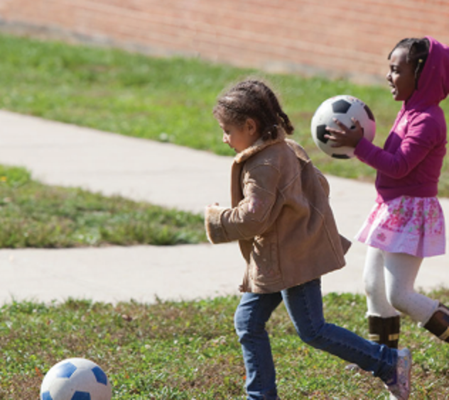 Two kids play outside and each has a soccer ball.