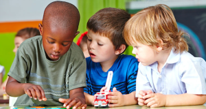 Three children sitting at a table are paying close attention to a puzzle in front of them.