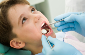 A young boy getting a dental checkup; there are dental tools in his mouth.