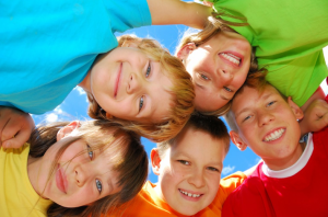 Five children standing with their arms around each other are looking down and smiling.