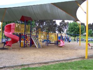 An outdoor playground sits under a gazebo, protected from sunlight.