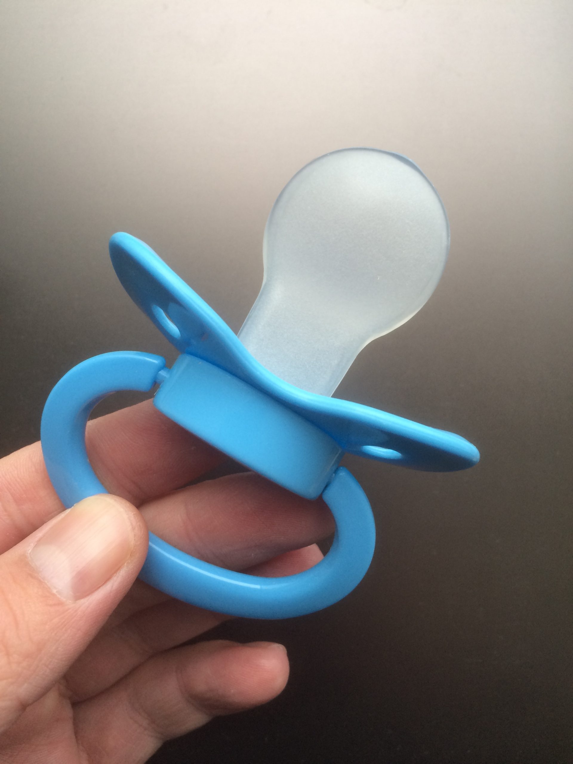 A blue pacifier in front of a grey background.