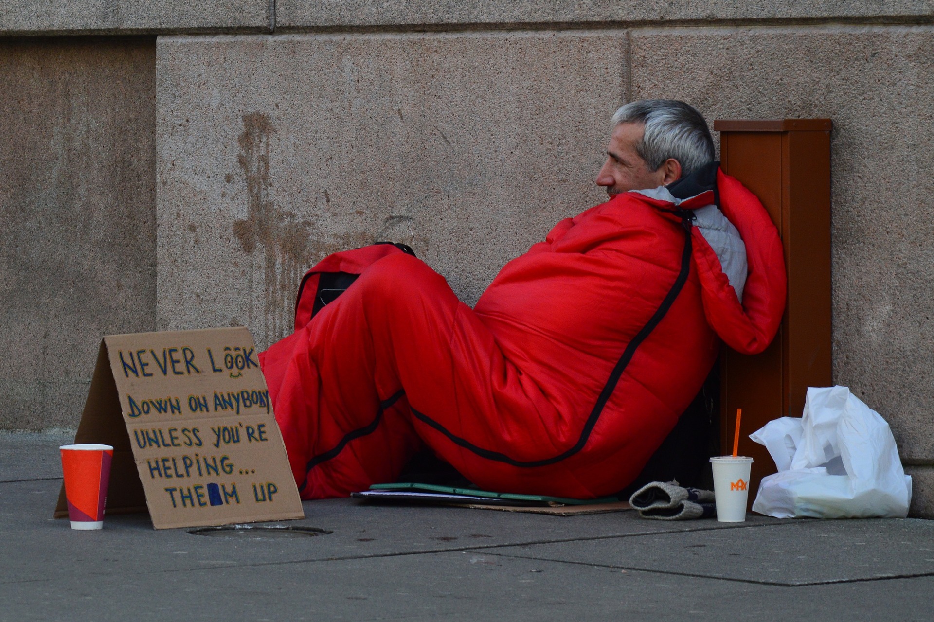 Homeless man in sleeping bag next to a sign