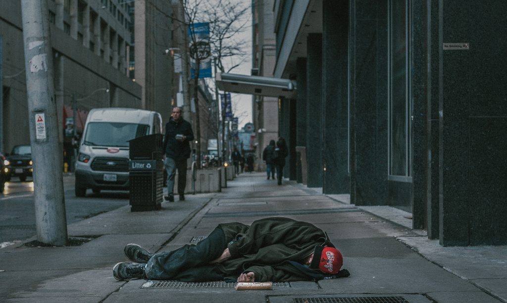 Photo of man lying on the sidewalk in an urban city.